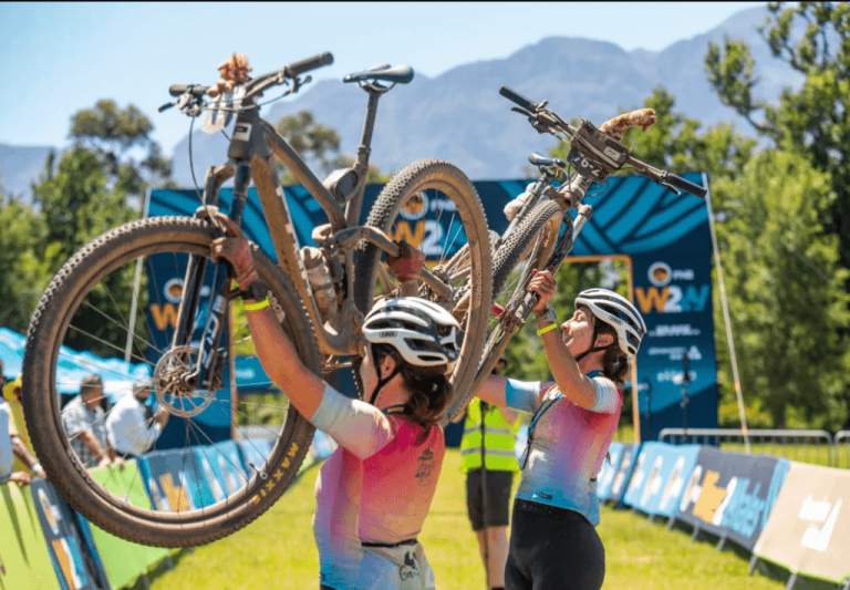 Two bikers holding their bikes over their heads