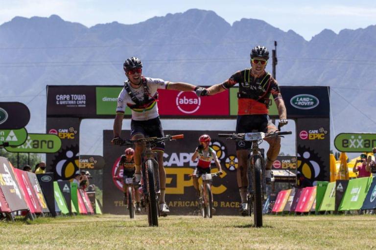 Beers and Sarrou holding hands across the  finish line while riding bikes