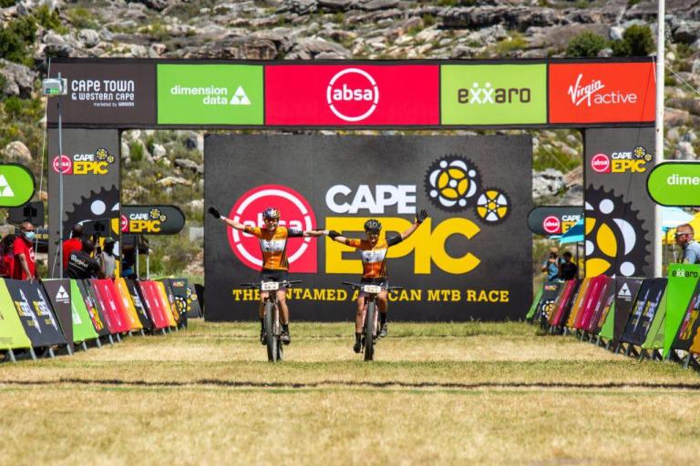 Stigger and Frei crossing the finish line holding hands while still on their bikes