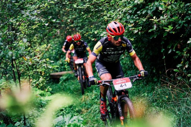 Three bikers wearing burnt orange helmets biking through a forest