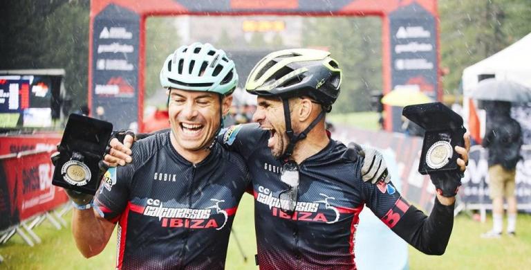 Two bikers in the rain showing their 2020 Swiss Epic Medals