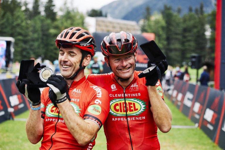 Two other bikers not in the rain wearing orange and showing off their medals
