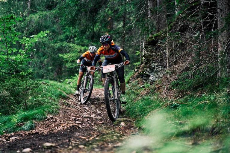 Two bikers heading down a forest path