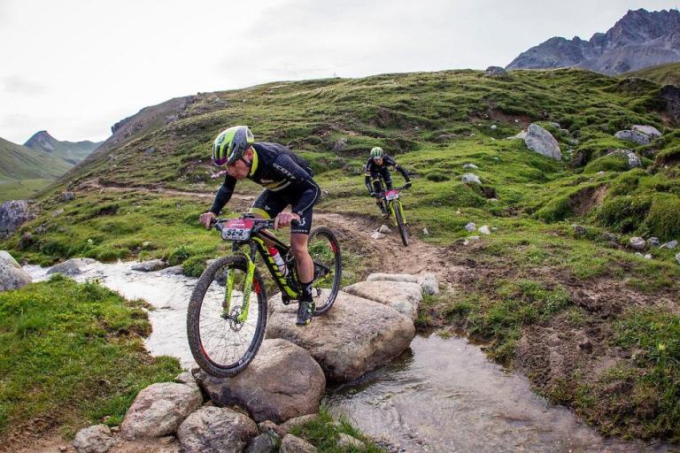 Two bikers heading over a creek with a rock bridge