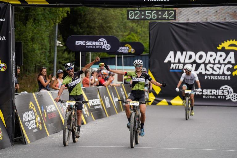 Two bikers fist bumping across the finish line, the time is 2:56:42
