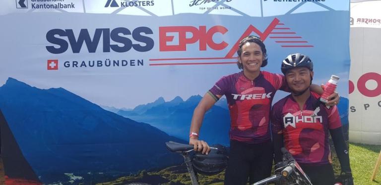 Two bikers posing by the Swiss Epic poster