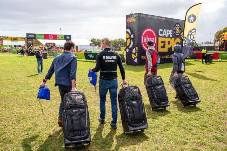 Four bikers pulling suitcases across grass