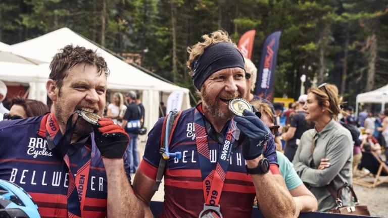 A pair of bikers biting their medals after a race [Swiss Epic]