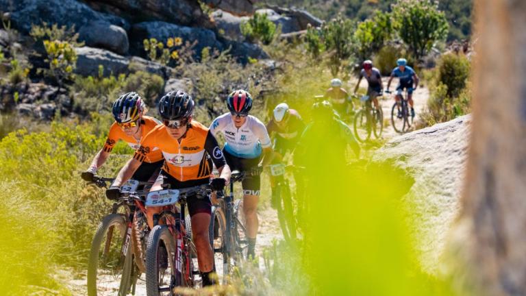 A shot through the bushes of Frei and Stigger leading the pack on the Absa Cape Epic [Epic Series]