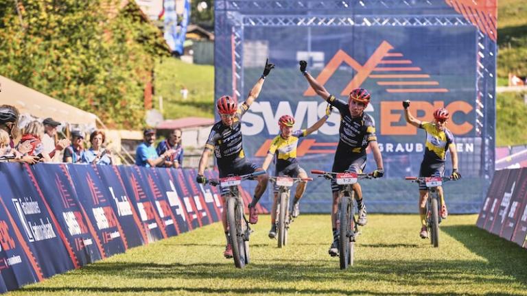 Four bikers crossing the swiss epic line with fists in the air [Swiss Epic]