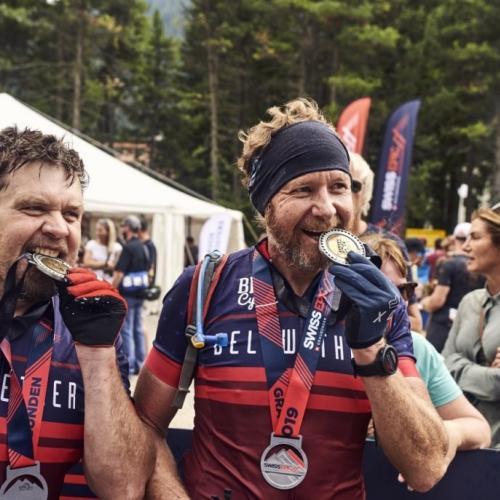 Two bikers biting their Swiss Epic Medals [Swiss Epic]